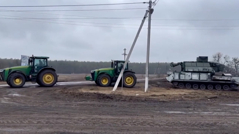 Two tractors tow away an abandoned missile launcher in Ukraine.