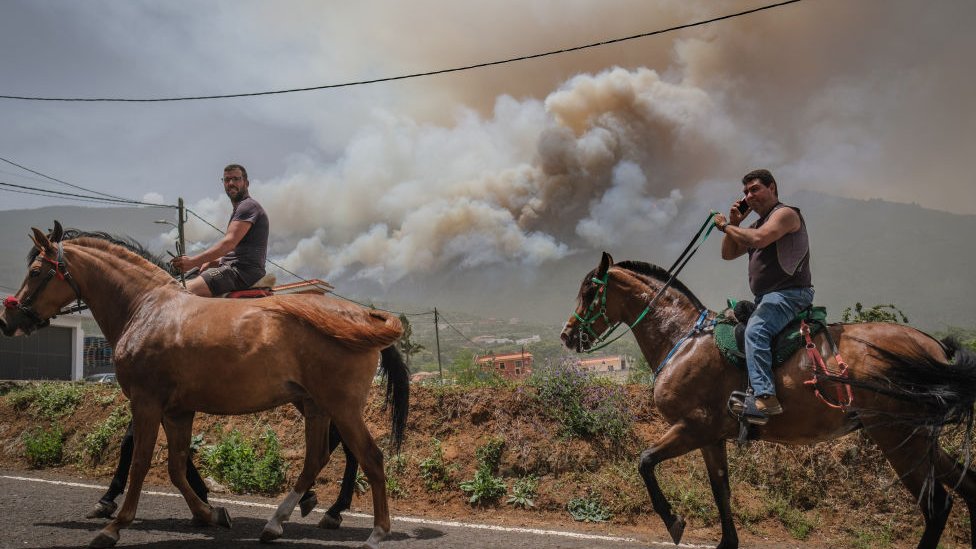 Two men on horseback, with smoke seen behind them.