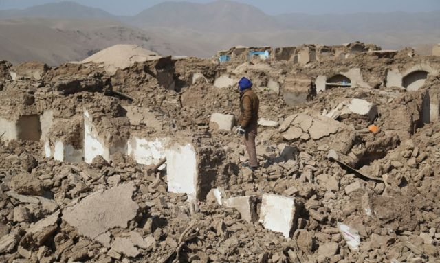 A man stands amidst collapsed homes 