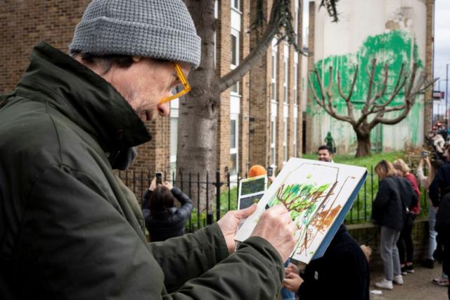 The Banksy mural from further away, where the green paint appears as foliage