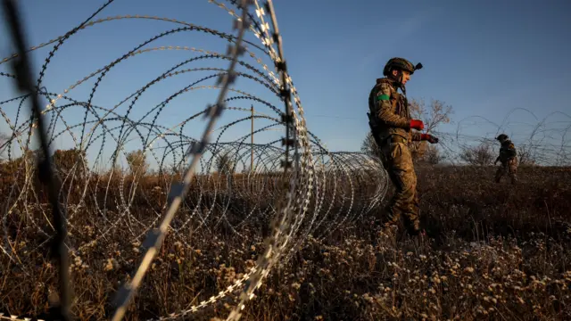 Двое военных в поле около колючей проволоки.