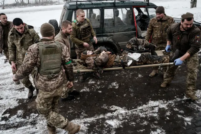 Эвакуация раненого. Несколько мужчин в военной форме несут на носилках еще одного.