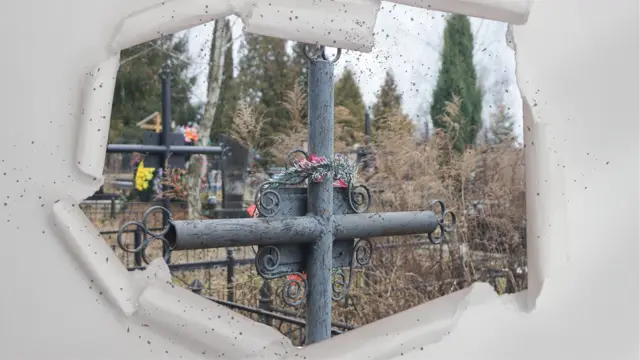 «Папу похоронили в огороде, где росли розы». Как разделенные фронтом украинские семьи часто не могут попрощаться с родными 6 Коллаж: в разорванное бумажное отверстие видны могилы на кладбище с металлическими крестами и оградками