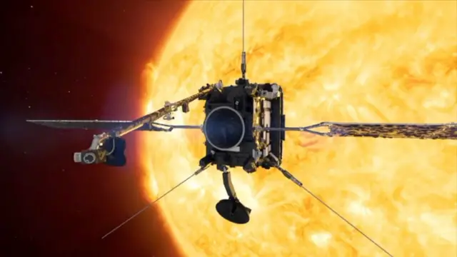 Космический аппарат, похожий с виду на серую коробку с антеннами, торчащими вверх и направленными по диагонали наружу из нижних углов, и двумя солнечными панелями, выступающими с каждой стороны. За ним видно ярко-желтое Солнце.
