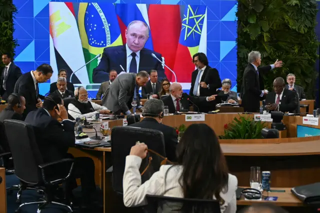 Путин на большом экране и люди, сидящие за круглым столом.