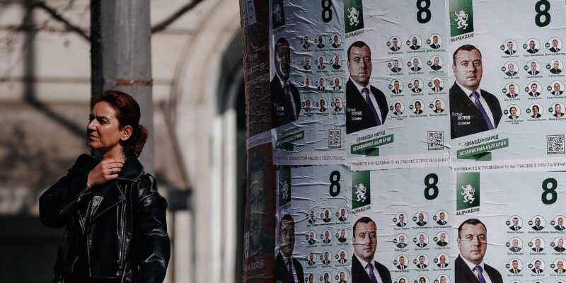 Женщина в Софии идет мимо расклеенных предвыборных плакатов в апреле 2026 года