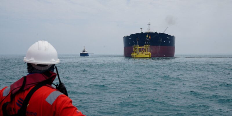 Сотрудник порта смотрит на нефтяной танкер, пришвартованный в море у нефтяного терминала