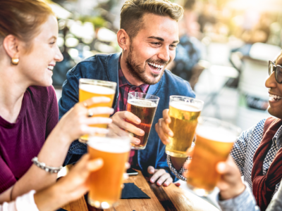 Компания смеющихся молодых людей с пивом в руках за столом в пабе