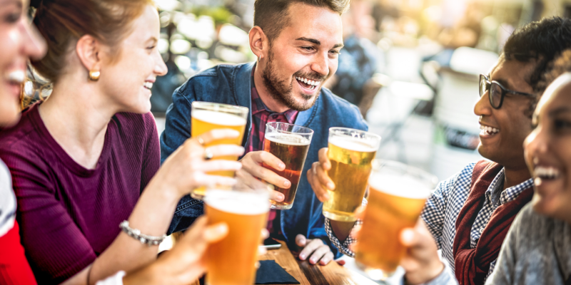 Компания смеющихся молодых людей с пивом в руках за столом в пабе