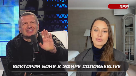 Скриншот из эфира, на одной половине улыбается Владимир Соловьев, поднося руку (на указательном пальце — пластырь) к микрофону, на другой половине Виктория Боня.
