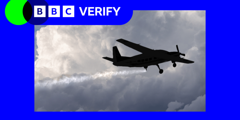 Небольшой самолет летит на фоне плотных серых облаков, распыляя мелкие частицы, которые образуют длинный белый след.