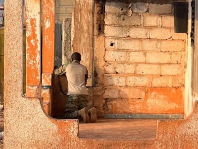 Мужчина в камуфляже с оружием стоит на коленях в кирпичном здании и наблюдает в окно