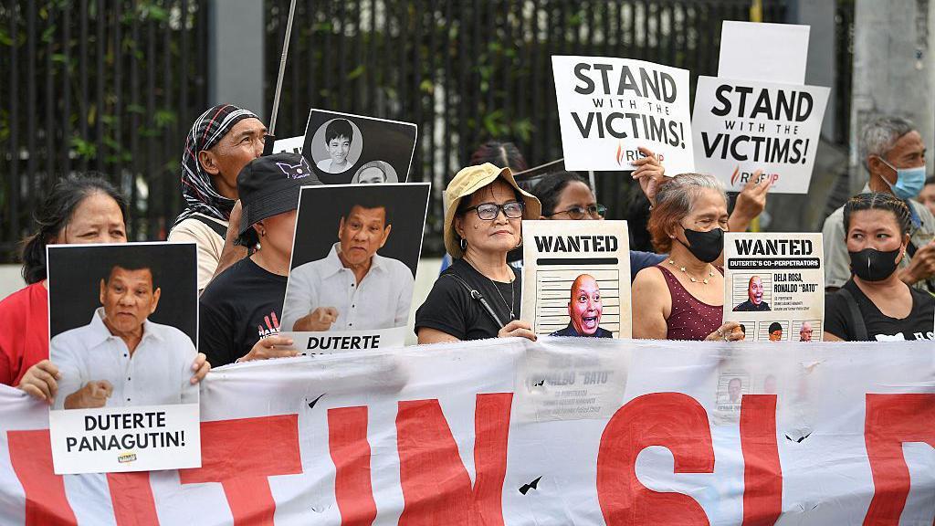 Родственники подозреваемых в наркоторговле, которые, как утверждается, были незаконно убиты по приказу бывшего президента Филиппин Родриго Дутерте, держат портреты Дутерте и его предполагаемых соучастников во время митинга на одной из улиц Манилы 11 марта 2026 года — в первую годовщину ареста бывшего президента и его передачи в Международный уголовный суд (МУС), расположенный в Нидерландах.