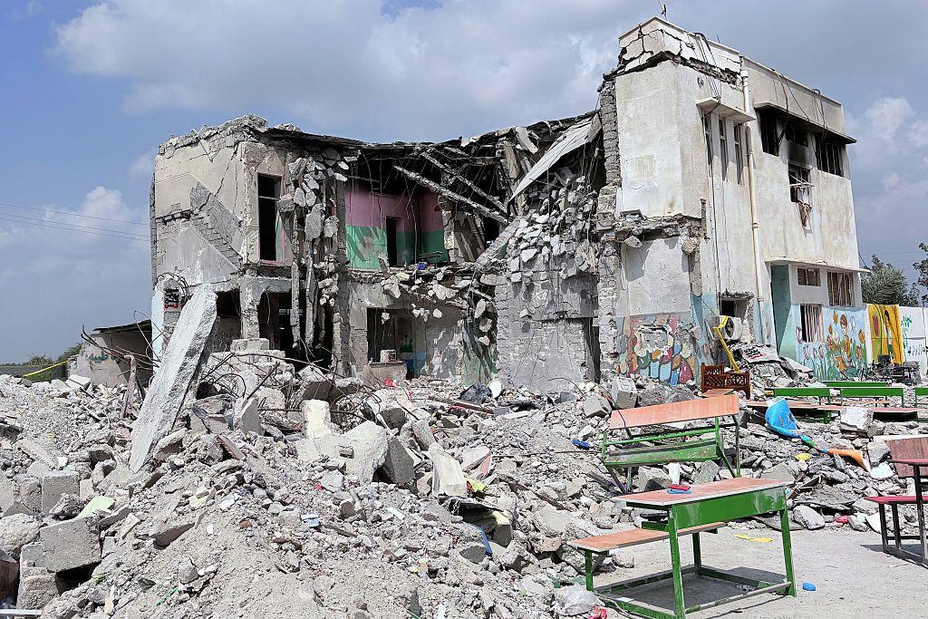 Развалины здания, возле которого стоят школьные парты.