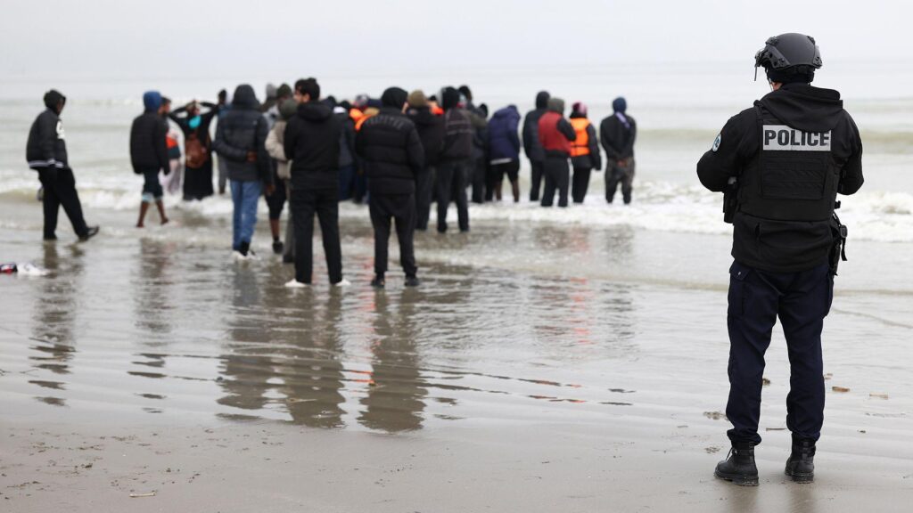 A police officer looks out to sea as a group of people wearing inflatable jackets stand in shallow water in Gravelines earlier this month.