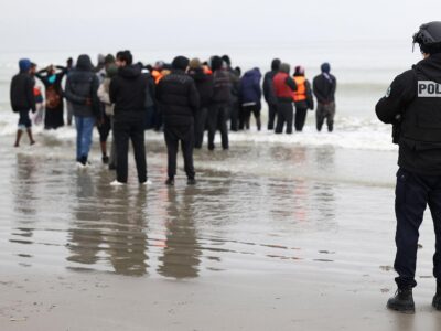 A police officer looks out to sea as a group of people wearing inflatable jackets stand in shallow water in Gravelines earlier this month.