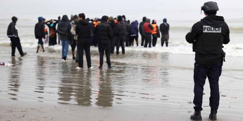 A police officer looks out to sea as a group of people wearing inflatable jackets stand in shallow water in Gravelines earlier this month.