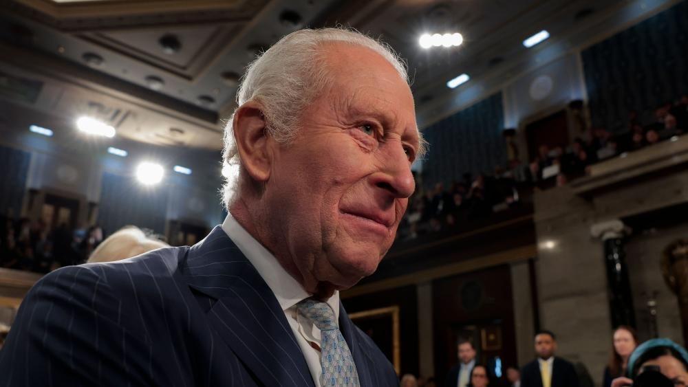 Король Карл в синем костюме в тонкую полоску, белой рубашке и светло-голубом галстуке.