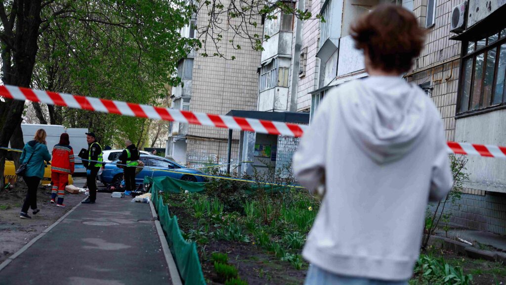 Мальчик в белой кофте смотрит на оцепленное место преступления у подъезда многоэтажки