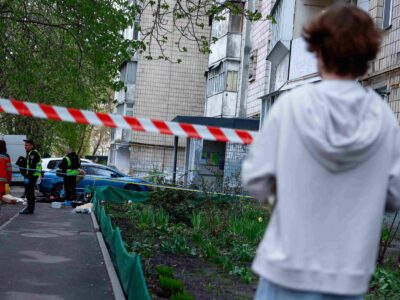 Мальчик в белой кофте смотрит на оцепленное место преступления у подъезда многоэтажки