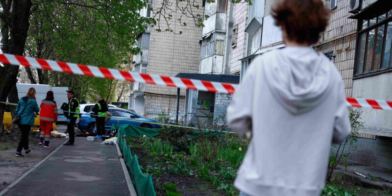 Мальчик в белой кофте смотрит на оцепленное место преступления у подъезда многоэтажки