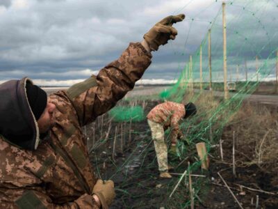 Двое украинских военных натягивают антидроновую сетку на столбах вдоль дороги