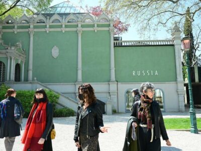 Четыре женщины, две из них в медицинских масках, идут по территории биеннале у павильона с надписью Russia.