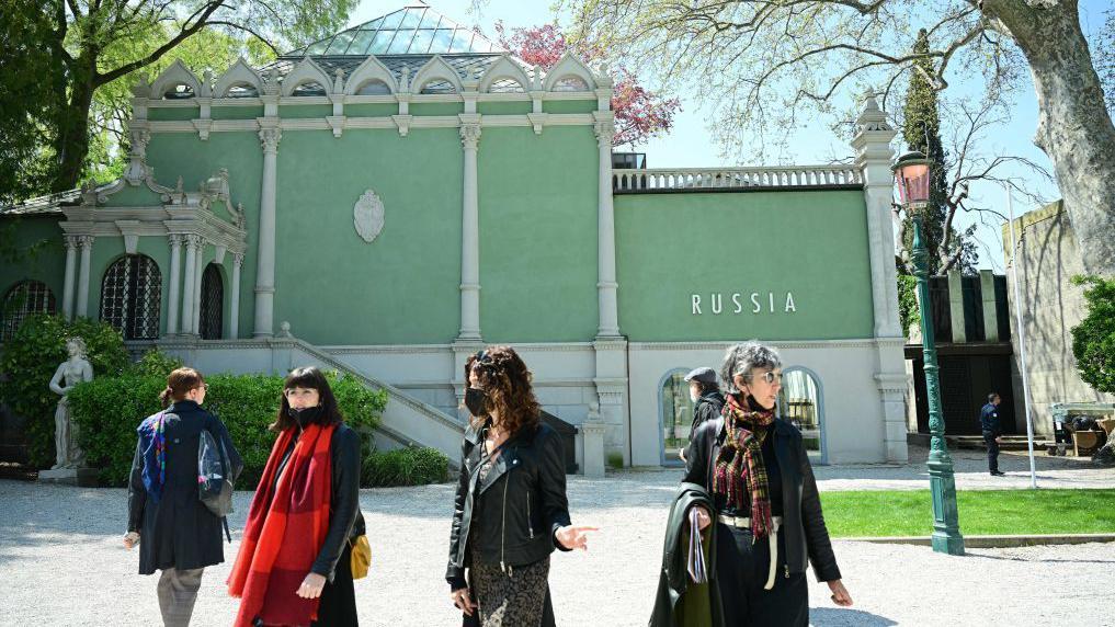 Четыре женщины, две из них в медицинских масках, идут по территории биеннале у павильона с надписью Russia.