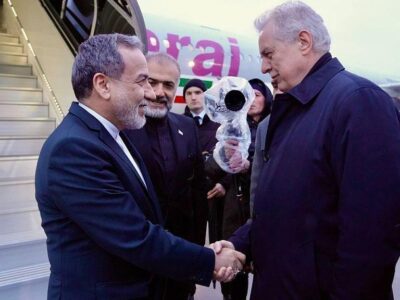 Двое мужчин пожимают друг другу руки у трапа самолета, на борту которого изображен флаг Ирана.