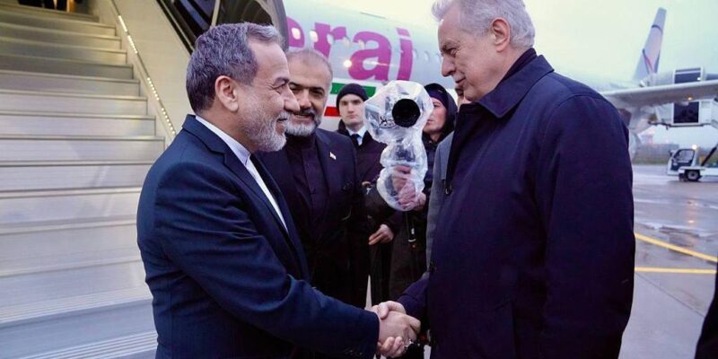 Двое мужчин пожимают друг другу руки у трапа самолета, на борту которого изображен флаг Ирана.