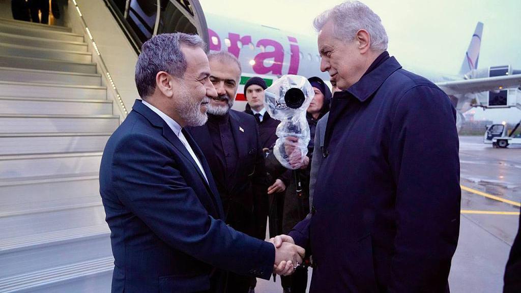 Двое мужчин пожимают друг другу руки у трапа самолета, на борту которого изображен флаг Ирана.