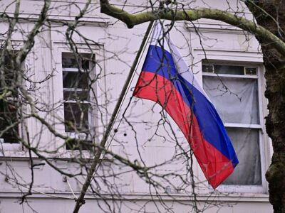 Российский флаг на здании за ветками деревьев.
