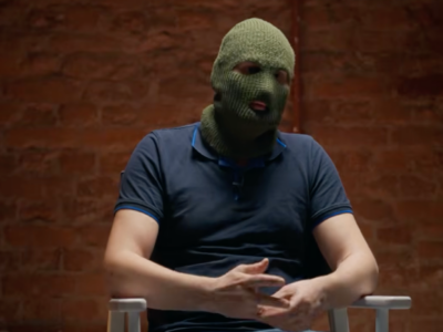 Мужчина в балаклаве сидит на стуле.