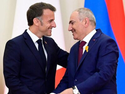 Макрон (слева) и Пашинян (справа), оба в темно-синих костюмах улыбаются и жмут друг другу руки
