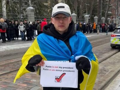 «У него два пути: тюрьма, фронт». Антивоенного активиста выдворяют из Финляндии в Россию 4 Роман Голиков стоит на улице с флагом Украины на плечах и плакатом с надписью «Putin is not my president»