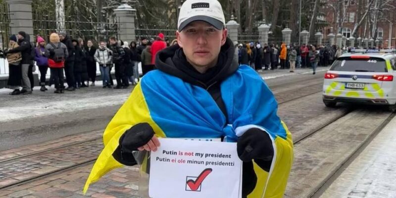 «У него два пути: тюрьма, фронт». Антивоенного активиста выдворяют из Финляндии в Россию 1 Роман Голиков стоит на улице с флагом Украины на плечах и плакатом с надписью «Putin is not my president»