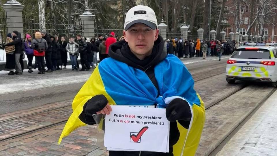 «У него два пути: тюрьма, фронт». Антивоенного активиста выдворяют из Финляндии в Россию 1 Роман Голиков стоит на улице с флагом Украины на плечах и плакатом с надписью «Putin is not my president»