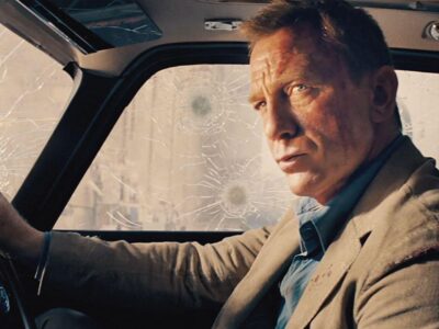 Daniel Craig sits in a car covered in gunshot impacts as he plays James Bond in the 2020 film No Time to Die
