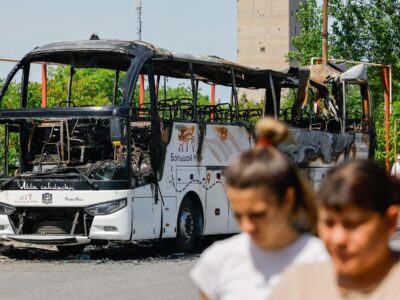 Две женщины идут по улице, за ними — сгоревший автобус.