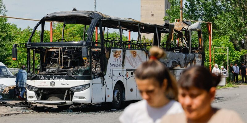 Две женщины идут по улице, за ними — сгоревший автобус.