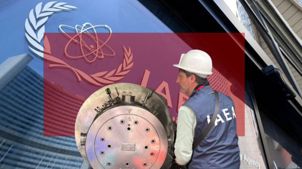 Человек в белой защитной каске и синем жилете с белыми буквами IAEA («МАГАТЭ») на спине. Он стоит рядом с металлическим цилиндром.