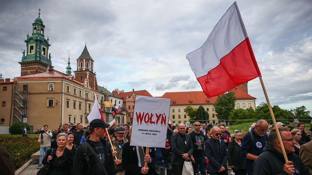 Люди идут с флагами Польши, на транспаранте на переднем плане написано Wołyń, буквы написаны красным и с них стекает кровь