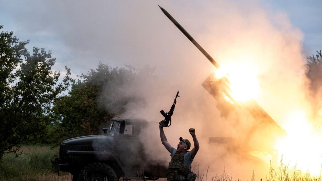 Наступил ли перелом в войне России с Украиной? 1 Военный вздымает в воздух автомат на фоне установки "Град", стреляющей ракетой