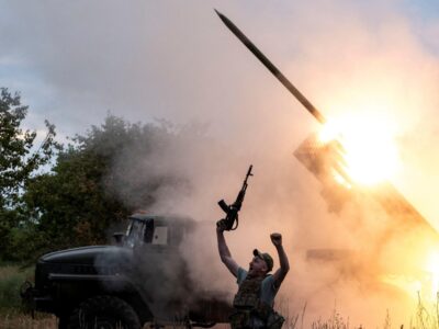 Наступил ли перелом в войне России с Украиной? 2 Военный вздымает в воздух автомат на фоне установки "Град", стреляющей ракетой