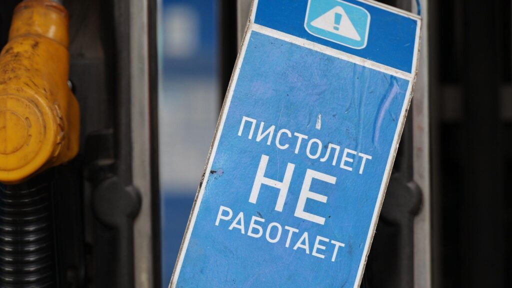 На заднем плане - заправочные пистолеты на заправке. На переднем плане синяя табличка с белой надписью "Пистолет не работает"