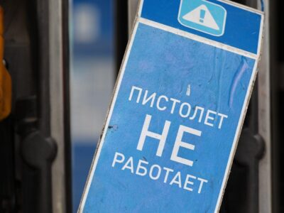 На заднем плане - заправочные пистолеты на заправке. На переднем плане синяя табличка с белой надписью "Пистолет не работает"