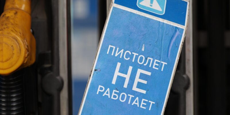 На заднем плане - заправочные пистолеты на заправке. На переднем плане синяя табличка с белой надписью "Пистолет не работает"
