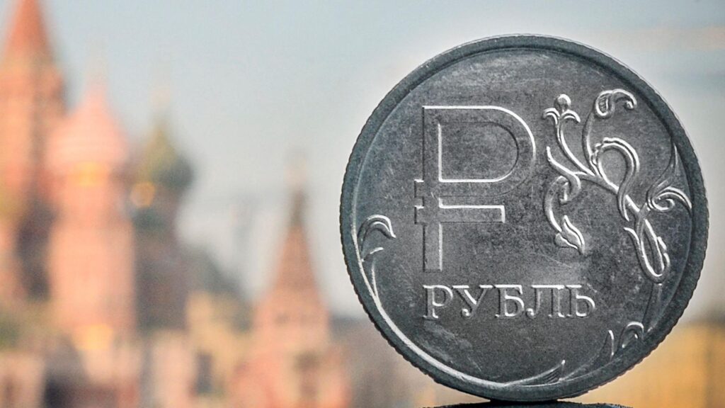 Период шоков. Как на российской экономике и бюджете отразится топливный кризис 1 На заднем плане размытые очертания православного собора Василия Блаженного в Москве. На переднем плане монета из серого металла с надписью "рубль"