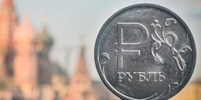 Период шоков. Как на российской экономике и бюджете отразится топливный кризис 11 На заднем плане размытые очертания православного собора Василия Блаженного в Москве. На переднем плане монета из серого металла с надписью "рубль"