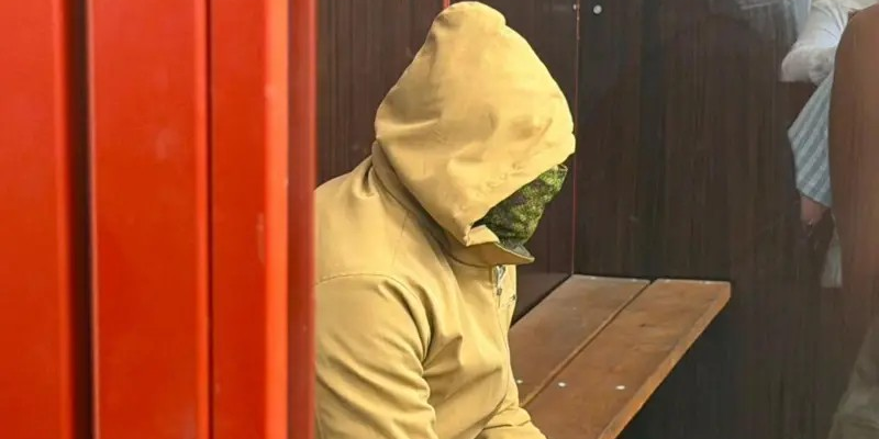 Покушение на бизнесмена Ермолаева в Монако: суд в Киеве арестовал сотрудника ГУР, подозреваемого в убийстве Березовской 1 Человек в светлом худи с капюшоном, лицо закрыто зеленой тканью. Он сидит на скамейке в стеклянном боксе в суде.
